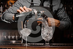 Barman pouring alcoholic drink into a glass using a jigger to prepare a cocktail