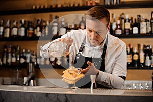 Barman pouring alcoholic drink mixed with ice into a glass