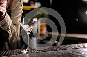 Barman pouring cold martini into glass on counter, closeup.