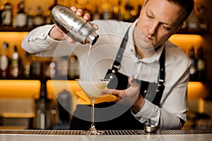 Barman pouring a fresh alcoholic drink into a cocktail glass