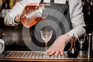 Barman pouring fresh alcoholic drink into the cocktail glass