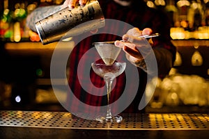 Barman pouring fresh alcoholic drink into an elegant glass