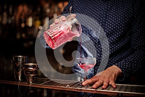 Barman pouring fresh and sweet pink summer cocktail into the glass