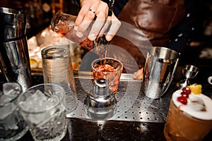 Barman is pouring out of a shaker into a crystal glass an alcoholic cocktail