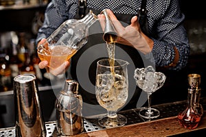 Barman pouring a portion of syrup from the bottle into the large cocktail glass