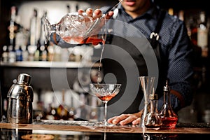 Barman pouring red alcoholic drink into the cocktail glass