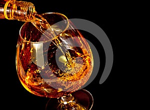 Barman pouring snifter of brandy in elegant typical cognac glass on black background