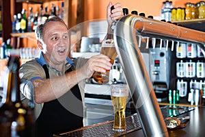 Barman is pouring unbottled beer with foam for client in the bar.