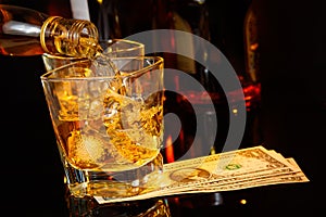 Barman pouring whiskey in front of whisky glass and bottles near dollars