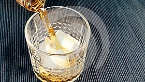Barman pouring whiskey in the glass with ice cubes on table, focus on ice cubes, whisky relax time on warm atmosphere