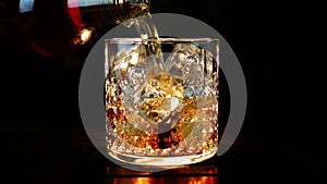 Barman pouring whiskey in the glass with ice cubes on wood table and black dark background, focus on ice cubes, whisky relax