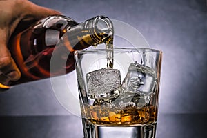 Barman pouring whiskey with ice cubes in glass on black background, cold atmosphere