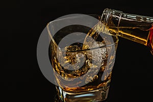 Barman pouring whiskey with ice cubes in glass on black background, cool atmosphere