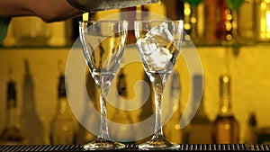 Barman puts cubes of ice into a glass, two glasses