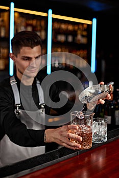 Barman puts the ice cubes into a glass with alcoholic drink