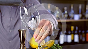 Barman puts ice on the wineglass for cocktail with lemon and rosemary. Hands close-up.