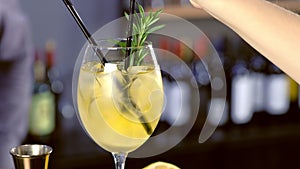 Barman puts straws in alcohol cocktail with sparkling wine, ice and liquor in wineglass, close-up view.