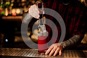 Barman putting big ice cube into a tomato bloody mary cocktail