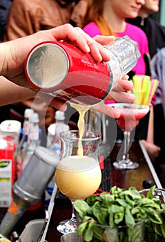 Barman's hand with shake mixer pouring cocktail into glass