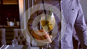 Barman serves a alcohol cocktail with sparkling wine, ice and liquor in wineglass, puts it on the table. Hands close-up.