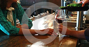 Barman serving red wine to female customer at bar counter