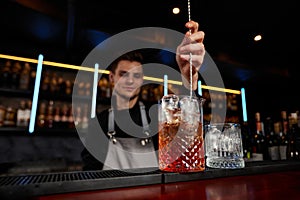 Barman stirring ice cubes in cocktail glass with spoon