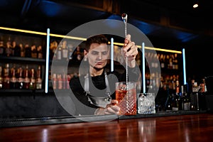 Barman stirring ice cubes in cocktail glass with spoon