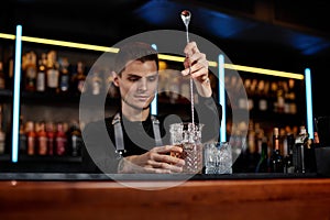 Barman stirring ice cubes in cocktail glass with spoon