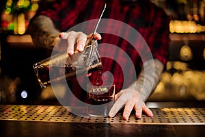 Barman pouring fresh strong alcoholic cocktail into a glass on bar