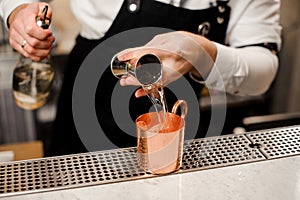 Barman in white shirt pouring a portion of alcoholic drink into a cup