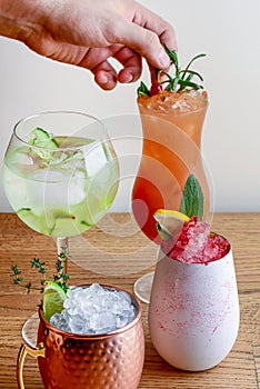 Barmans hand decorating four different assorted cocktail drinks made with alcohol and fruit served in unique glasses