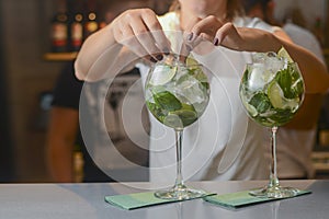 Barmans hand decorating two glasses of alcohol cocktail drinks arranged in a line. Bartender at work in bar.