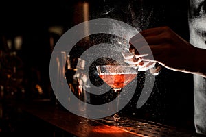 Barmans hands sprinkling the juice into the cocktail glass