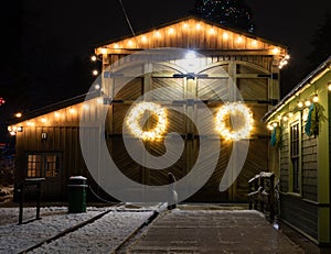 Barn house decorated with christmas lights photographed on a winter night, this wreath stands out against the weathered wooden