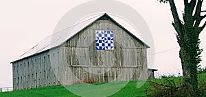 A barn with an ornamental barn quilt in a green horse field