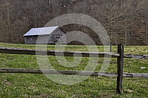 Barn and split rail fence during a snow flurry