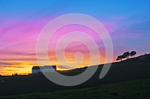 Barn and trees silhouette against sunset sky