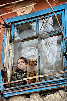 A girl with a dog in a poor quarter looking out the window of an old house