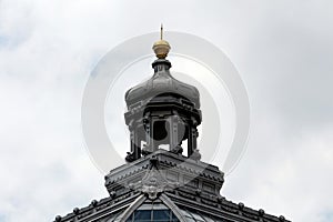 Baroque style dome with golden tip on top of old building with glass and metal roof tiles surrounded with various decorative