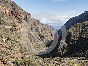 Barranco de Guayadeque with ravine steep walls and winding road towards ocean. Gran Canaria, Canary Island, Spain. Sunny