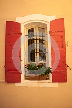 Barred window, with a planter and a pair of wood, red, shutters