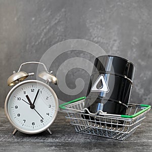 A barrel of oil in a grocery basket and an alarm clock. The concept of the dependence of the prices of raw materials for all