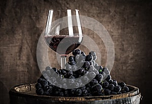 Barrel, wineglass with some red wine and ripe grapes of wine on