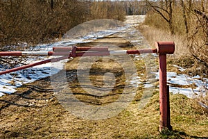 The barrier blocks the passage on a rural dirt road. Closed park area. The first snow on the dry grass along the roadside