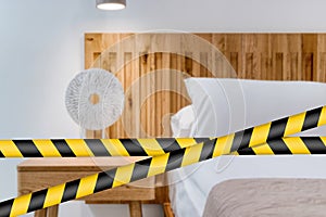 Barrier tape - quarantine, isolation concept, entry ban. Do not cross. View of detail a bed in a bedroom with a lamp and side