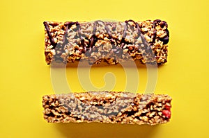 Bars of granola with chocolate and cranberries lie on the table of yellow color close-up view from above