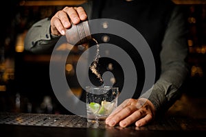 Bartender adding cane sugar into the cocktail glass with lime. P