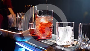 Bartender adding ice cubes and stirring in cocktail glass making cocktail in speakeasy bar
