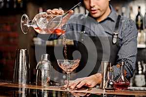 Bartender adding red alcoholic drink into cocktail glass