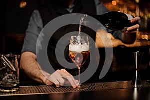 Bartender adds sparkling wine in cocktail on a bar counter